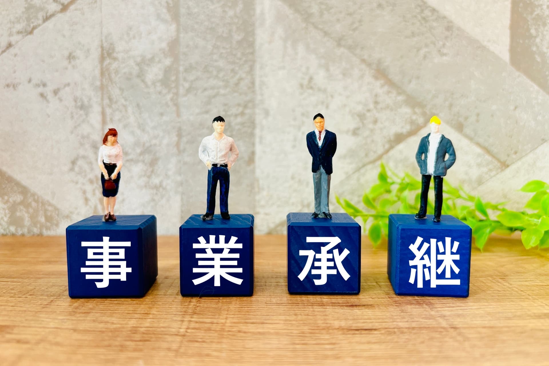 「事業承継」の文字ブロックの上に経営者や後継者を表すミニチュアフィギュアが並ぶ、事業承継をイメージした写真